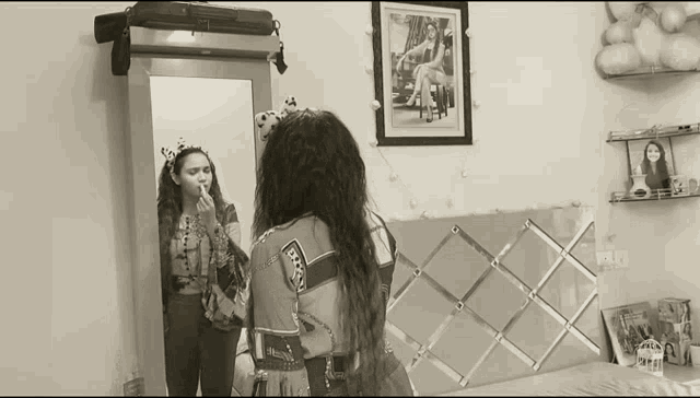 a woman applying makeup in front of a mirror with a picture on the wall behind her