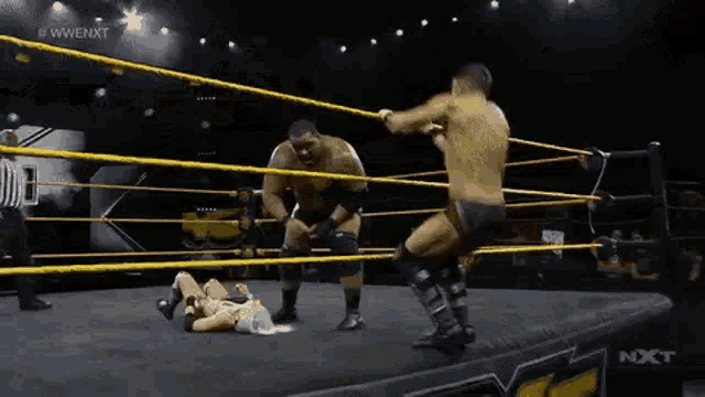two men are wrestling in a wrestling ring with a referee in the background .