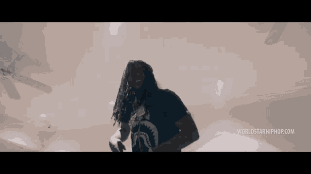 a man with long dreadlocks is dancing in a living room with a ceiling fan .