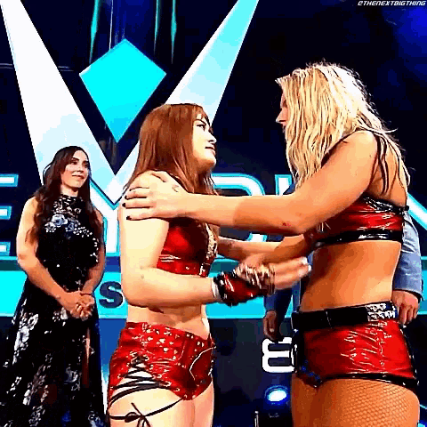 two women are hugging each other on a stage while a man stands behind them .