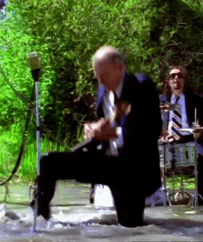 a man in a suit and tie is kneeling in a stream