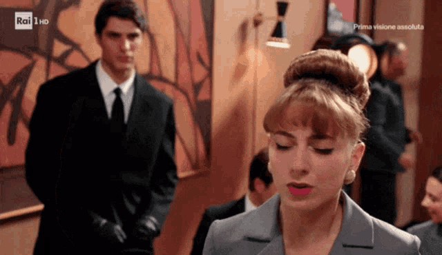 a man in a suit and tie stands in front of a woman in a grey suit and a sign that says rai 1 hd