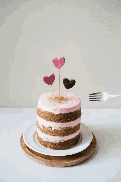 a naked cake with pink frosting and hearts on toothpicks