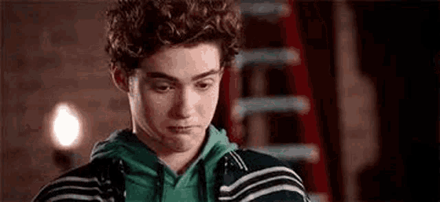 a young man with curly hair is standing in front of a ladder and making a funny face .