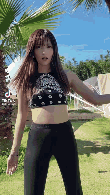 a woman in a crop top and black pants is standing in front of a palm tree ..