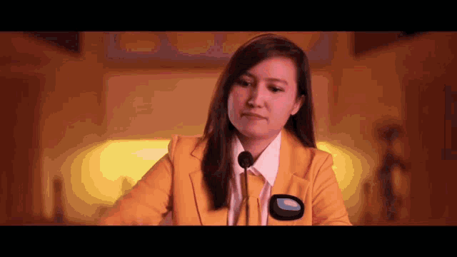 a woman in a yellow suit is sitting at a podium with a microphone .