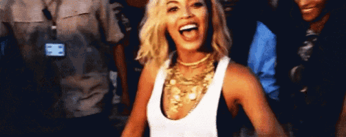 a woman wearing a white tank top and gold necklace is dancing in a crowd .