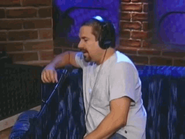 a man wearing headphones is sitting in front of a microphone and talking into it .