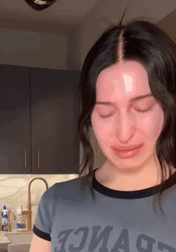 a woman is crying in a kitchen wearing a t-shirt that says " twice "
