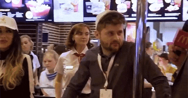 a man in a suit and hat is standing in a line at a mcdonald 's .