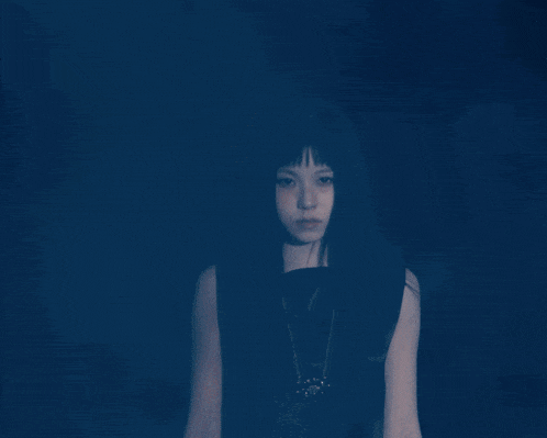 a woman with long black hair is wearing a black top and a necklace