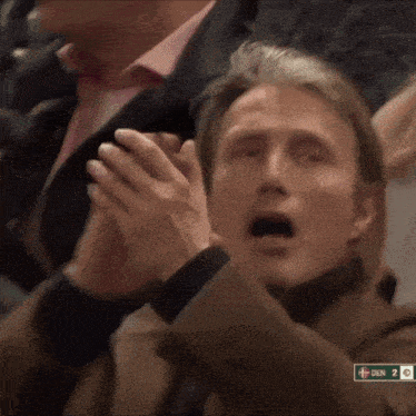 a man with his mouth open is clapping in a crowd with a sign that says den on it