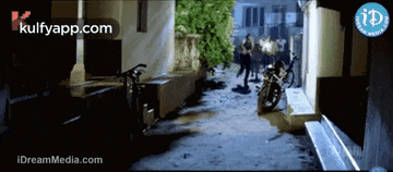 a motorcycle is parked in a narrow alleyway next to a building with the website kulfyapp.com on the bottom