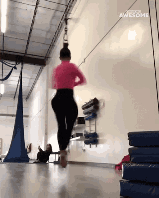 a woman in a pink top and black pants is jumping a rope in a gym with the words awesome above her