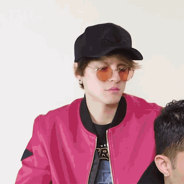 a man wearing sunglasses and a pink jacket with the letter r on the front