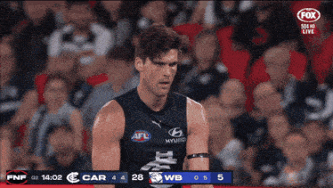 a man in an afl jersey stands in front of a scoreboard