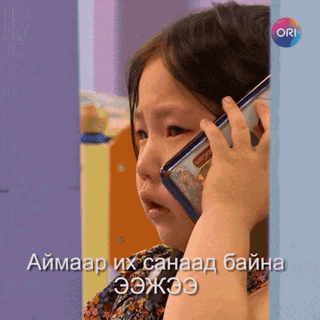 a little girl is crying while talking on a cell phone with ori in the corner