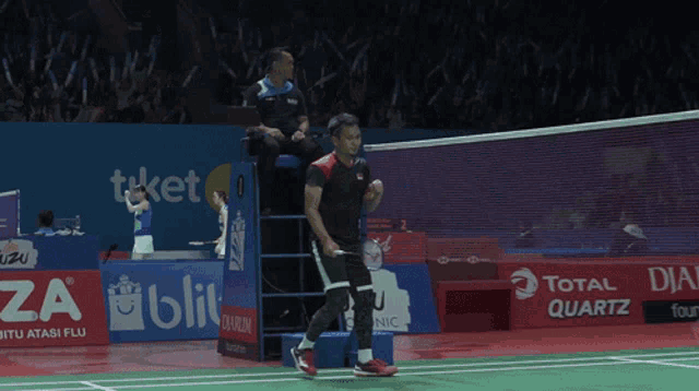 a man on a badminton court with a total quartz advertisement behind him