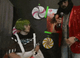 a man in a red jacket is holding a microphone and talking to a girl in a green wig