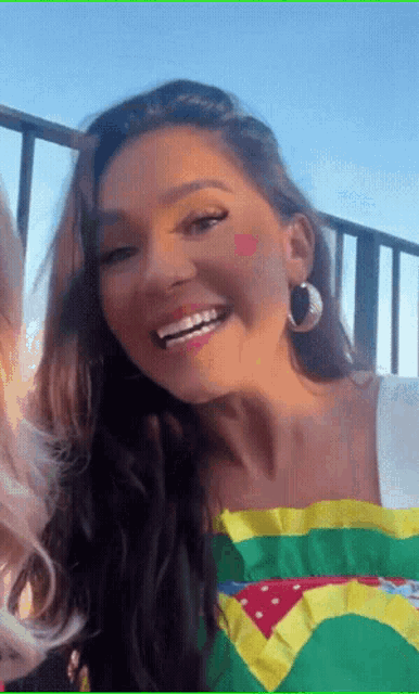 a woman wearing a brazilian flag shirt and hoop earrings smiles