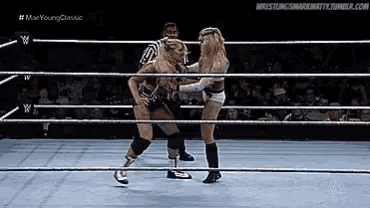 two women are wrestling in a ring with a referee in the background .