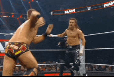 two men are fighting in a wrestling ring with the word raw on the ropes .