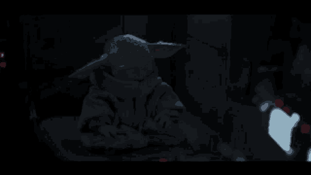 a baby yoda is sitting on a chair in the dark in a room .