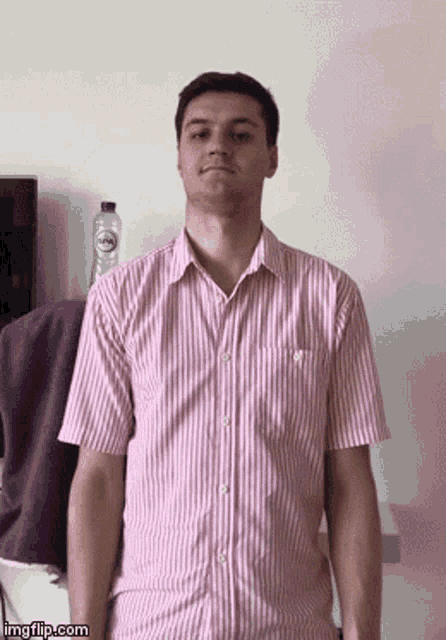 a man in a pink and white striped shirt stands in front of a bottle of water