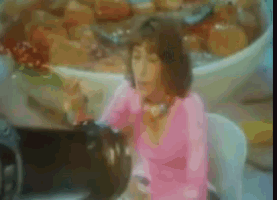 a woman in a pink shirt is sitting in front of a bowl of soup .