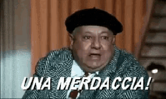a man wearing a beret and a suit is making a funny face and says una merdaccia !