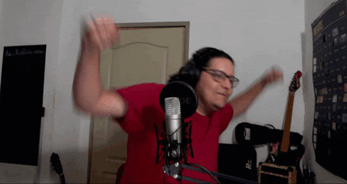 a man in a red shirt stands in front of a rode microphone with his arms outstretched
