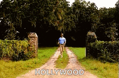a man is walking down a dirt road with the word hollywood on the side .