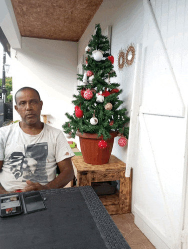 a man wearing a star wars shirt sits in front of a small christmas tree