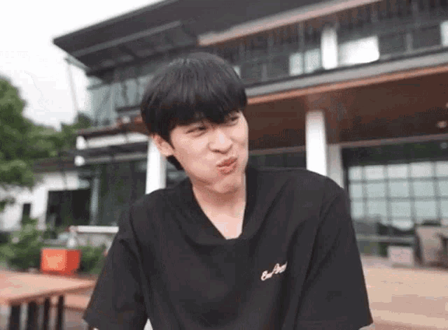 a young man in a black t-shirt is making a funny face in front of a large building .