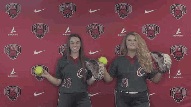 two female softball players pose in front of a cwu backdrop