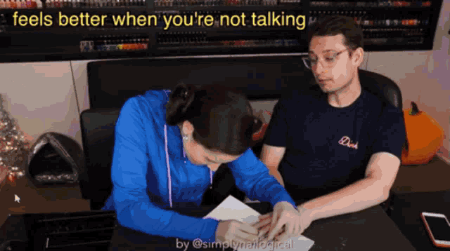 a man and a woman are sitting at a table and the woman is writing on a piece of paper
