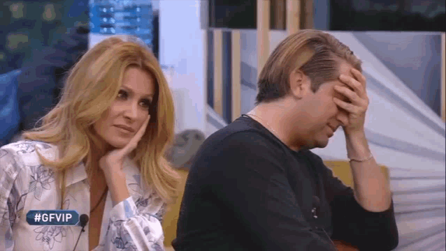 a man and a woman are sitting next to each other with the man covering his face .