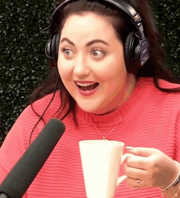 a woman wearing headphones holds a cup of coffee in front of a microphone