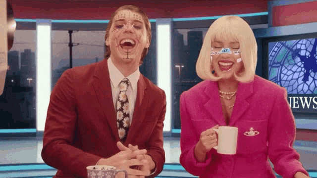 a man and a woman laughing in front of a news screen