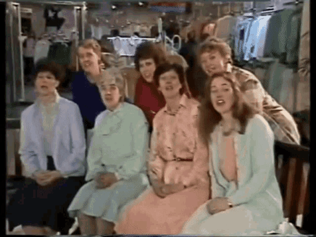 a group of women are sitting in front of a clothing rack