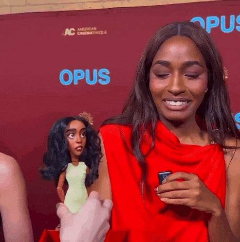 a woman in a red dress is smiling in front of a red background with opus written on it