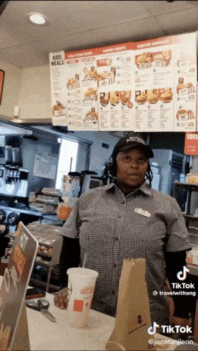 a woman behind a counter at a fast food restaurant with a menu above her