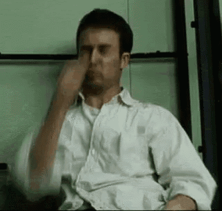 a man in a white shirt is sitting in a chair with his eyes closed and his hand on his nose .