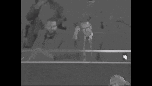 a man in a suit and tie is sitting in the stands of a stadium .