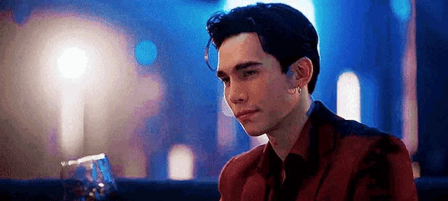 a young man in a red suit is sitting at a table with a glass of wine in front of him .