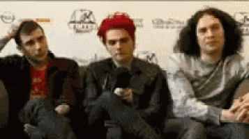 three men are sitting on a couch talking to each other .