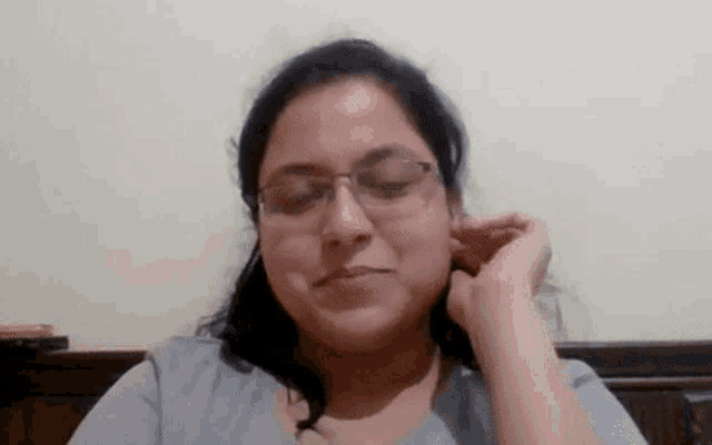 a woman wearing glasses is holding her hand to her ear and smiling .