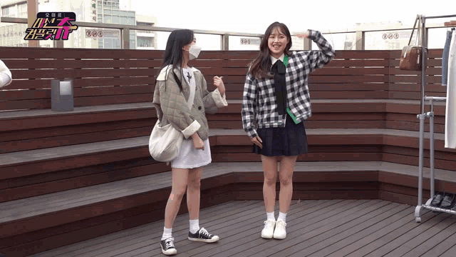 a girl wearing a mask stands next to another girl on a deck