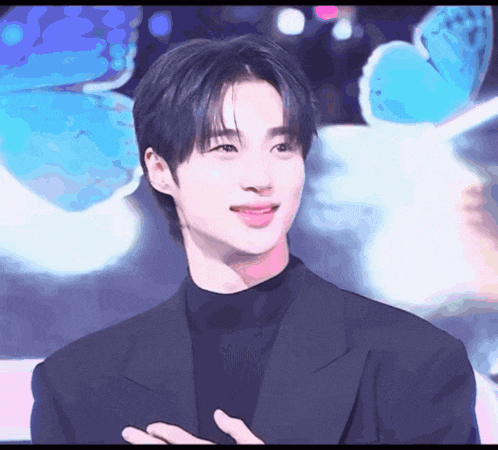 a young man wearing a black suit and turtleneck looks at the camera