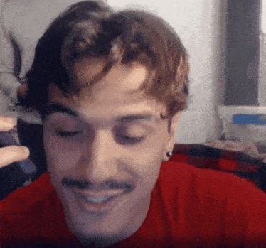 a man with a mustache is wearing a red shirt and smiling